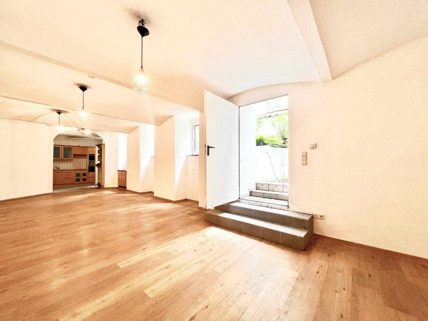 Heller Mehrzweckraum mit Holzboden und direktem Zugang zum Außenbereich über eine Treppe.