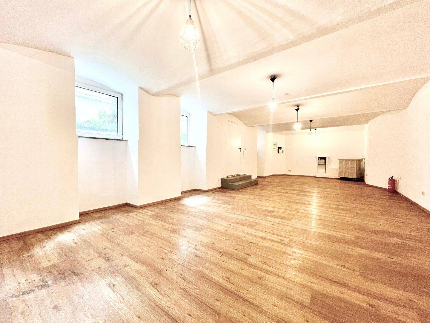 Großer, heller Mehrzweckraum mit Holzboden, gewölbter Decke und mehreren Fenstern.