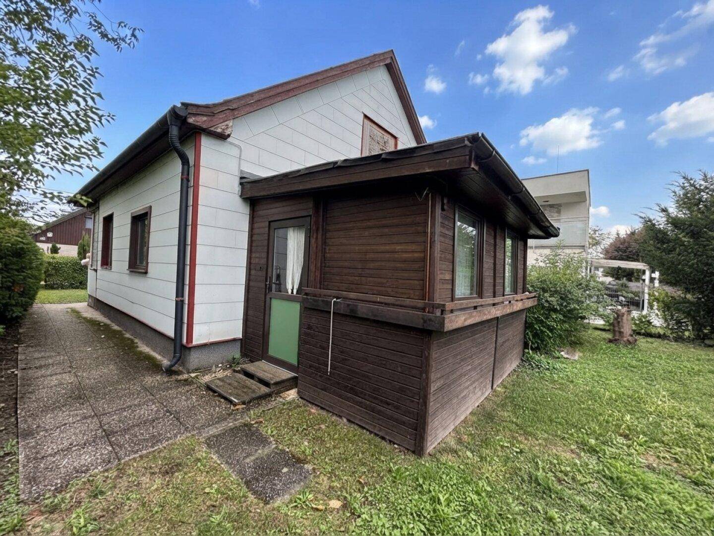 Seitenansicht des Hauses mit Holzveranda und einem gepflasterten Weg im Garten.