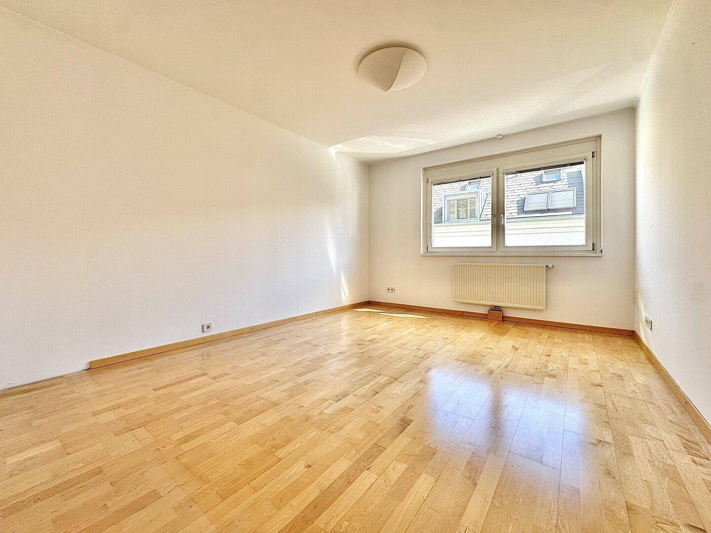 Lichtdurchflutetes Zimmer mit Parkettboden, Rollläden und weitem Blick über die Dächer.