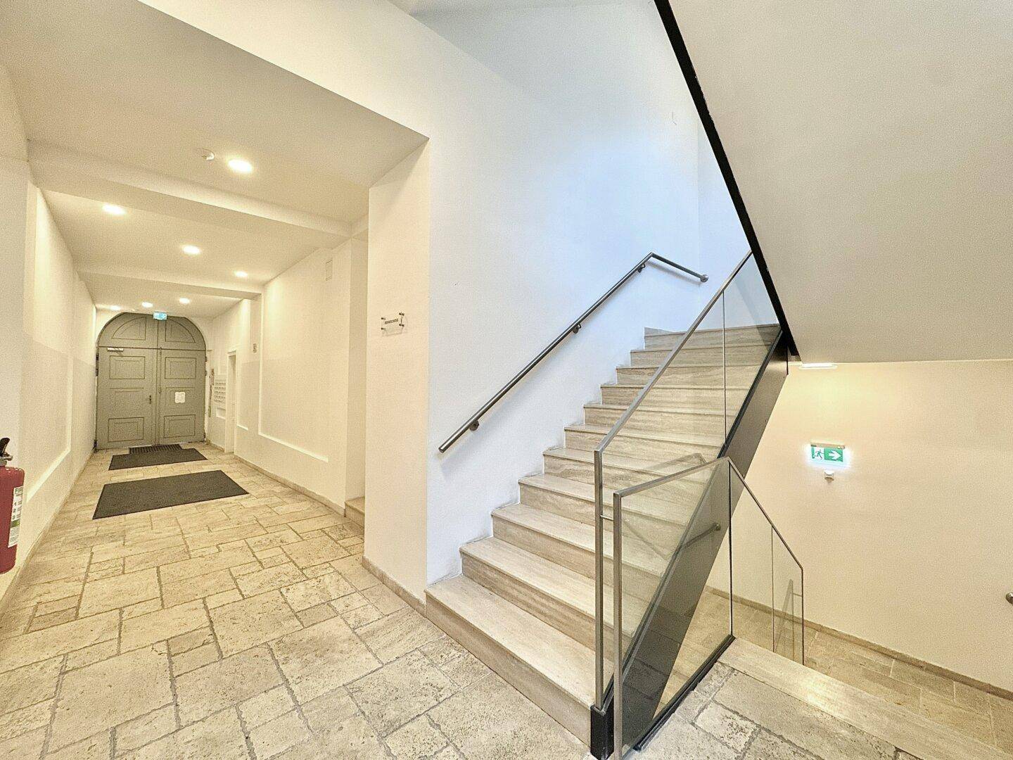 Heller Eingangsbereich mit moderner Treppe aus Glas und Edelstahl sowie Natursteinboden.