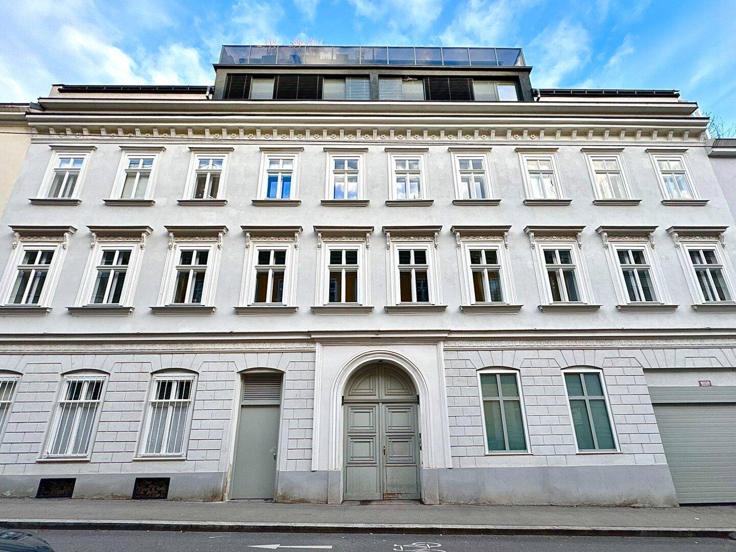 Klassische Fassade eines Altbaus mit vielen Fenstern und einem modernen Dachausbau.