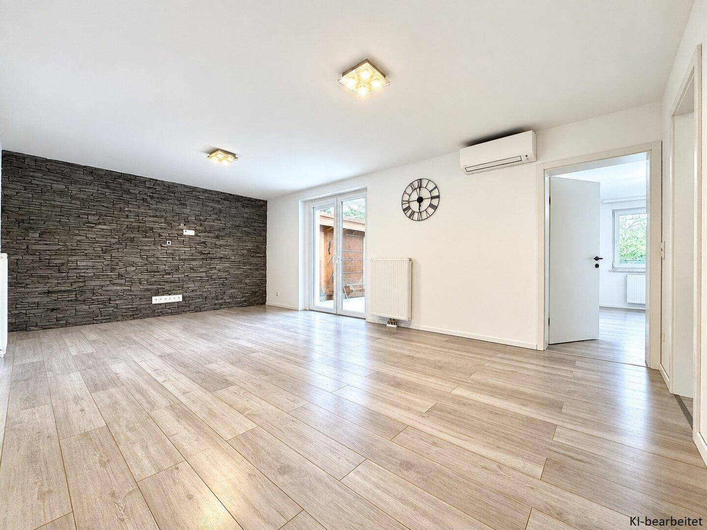 Heller, leerer Wohnraum mit moderner Steinwand, hellem Laminatboden und Zugang zum Außenbereich.