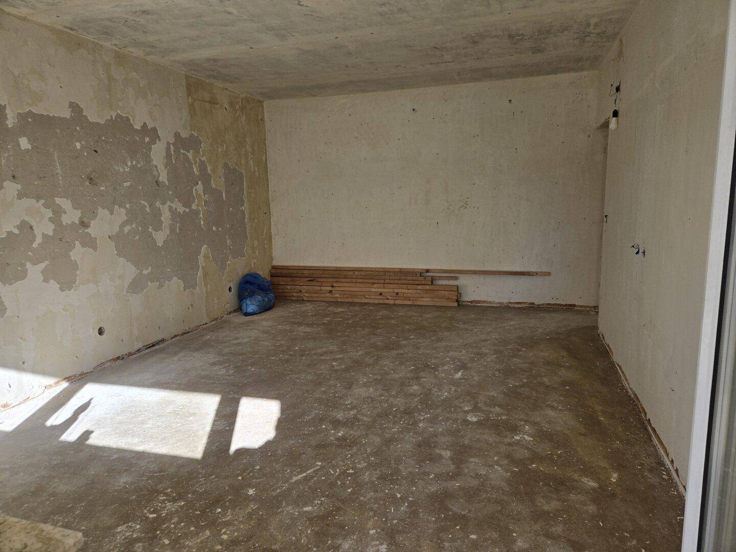 Unfertiger Raum im Rohbauzustand mit Betonboden und gelagerten Baumaterialien.