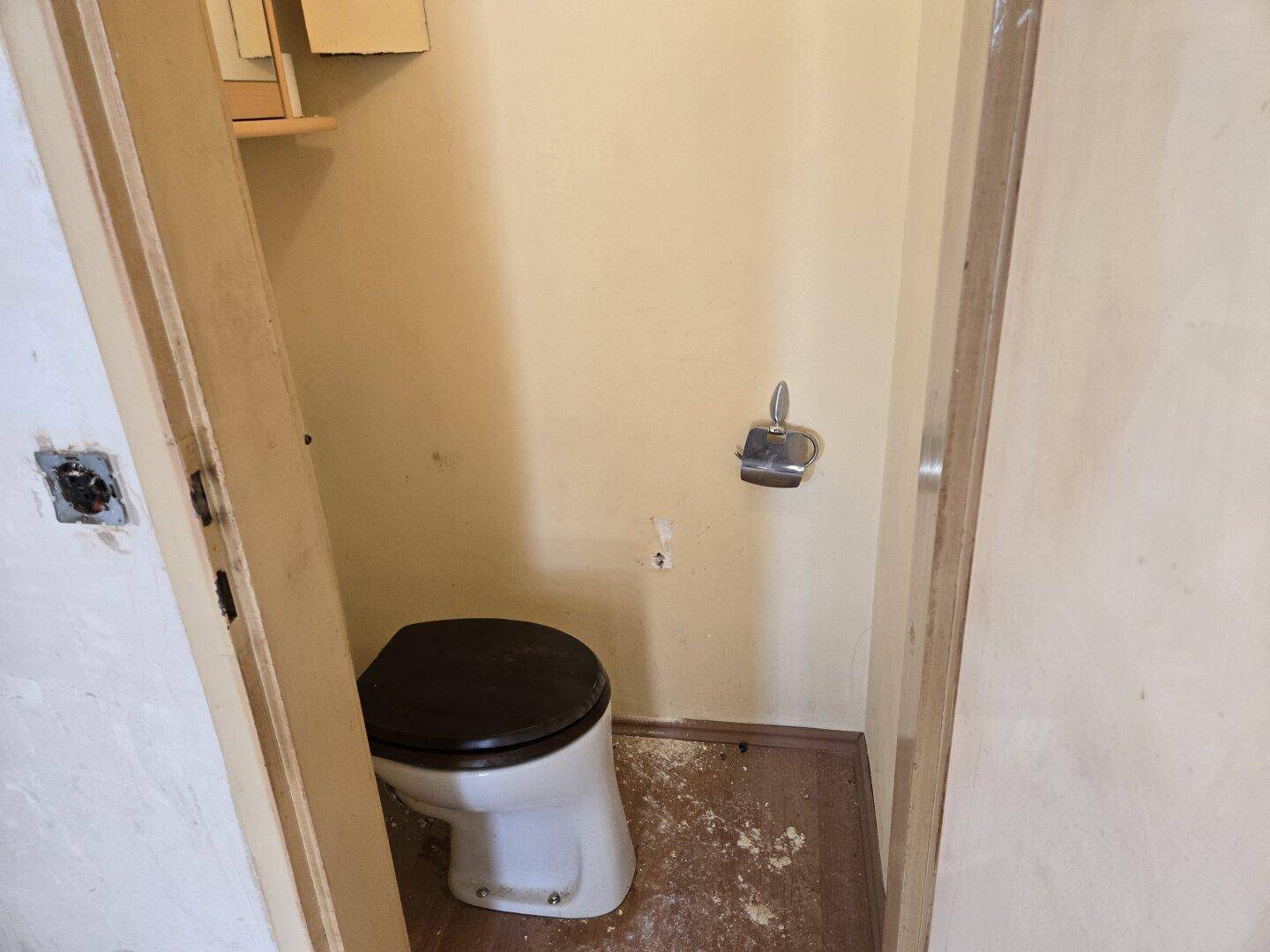 Kleines Gäste-WC mit einfacher Toilette und Toilettenpapierhalter, funktional und kompakt.
