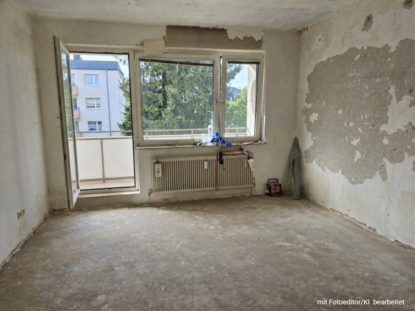 Geräumiges Zimmer im Rohbau mit Balkonzugang und Blick auf die umliegenden Gebäude und Bäume.