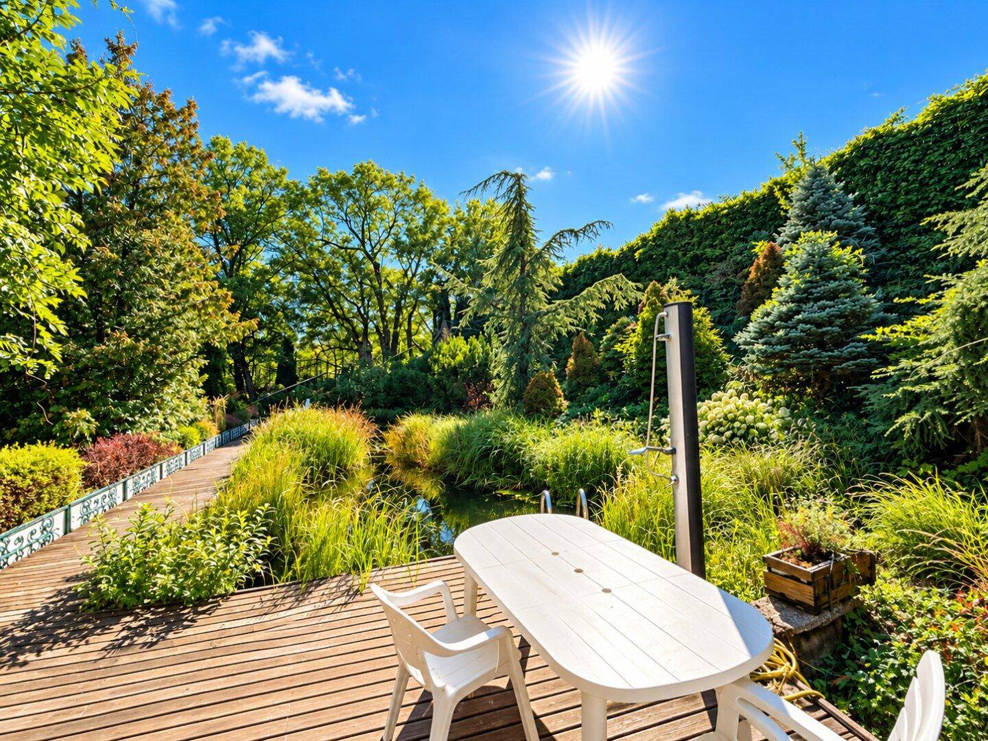 Helle Holzterrasse mit weißem Esstisch und Stühlen, bietet einen schönen Blick auf den Teich und den üppigen Garten.