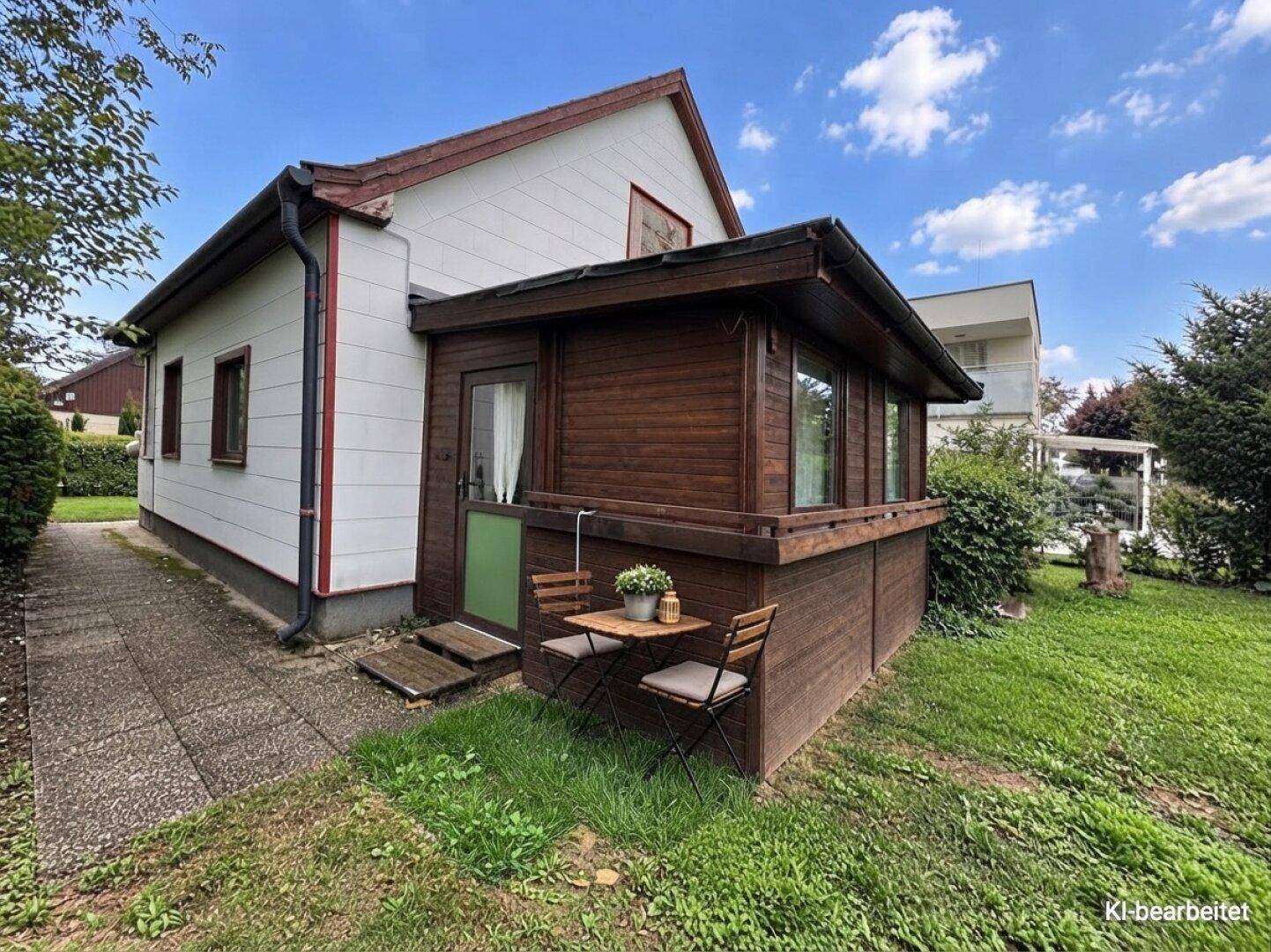 Gepflegtes Gartenhaus mit Holzverkleidung, Wintergarten und einer kleinen Sitzecke im Grünen.
