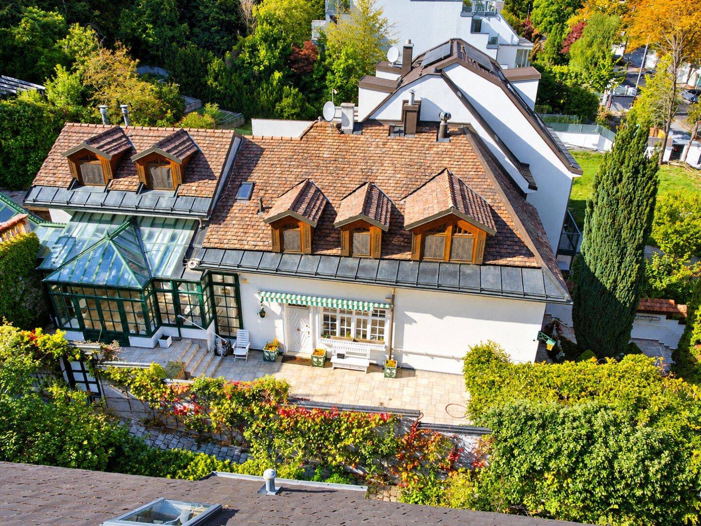 Nähere Luftaufnahme des Hauses mit Mansarddach, dem markanten Wintergarten und der einladenden Terrasse.