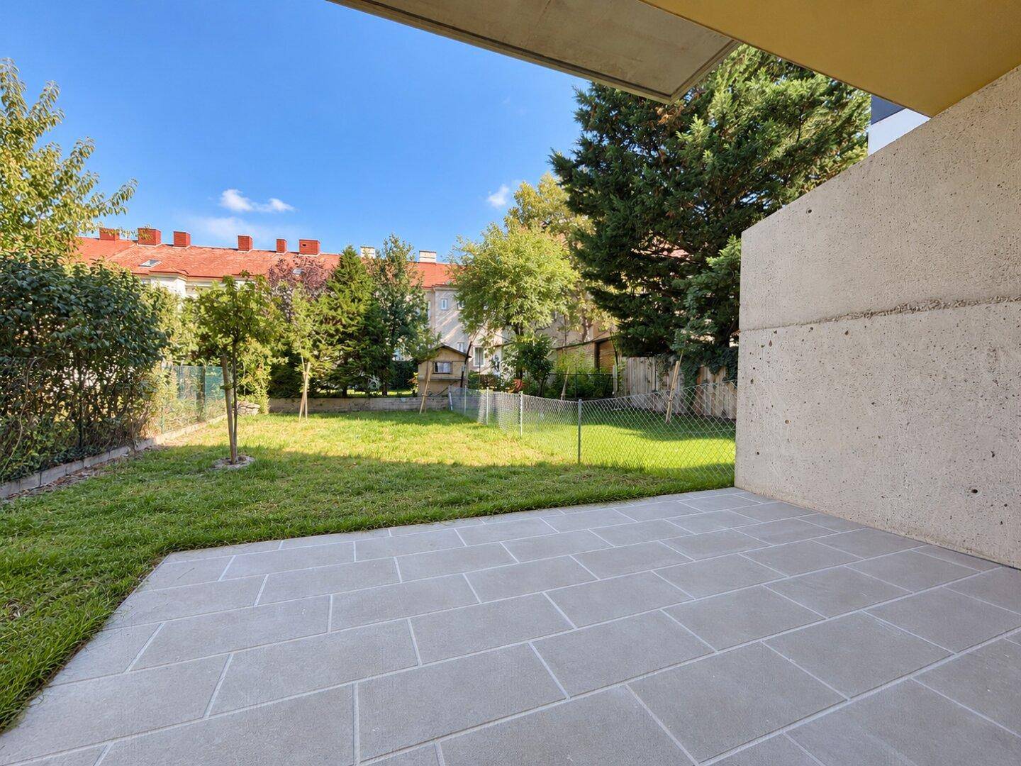 Geräumige Terrasse mit Blick auf den Garten und die umliegende Wohnbebauung unter blauem Himmel.