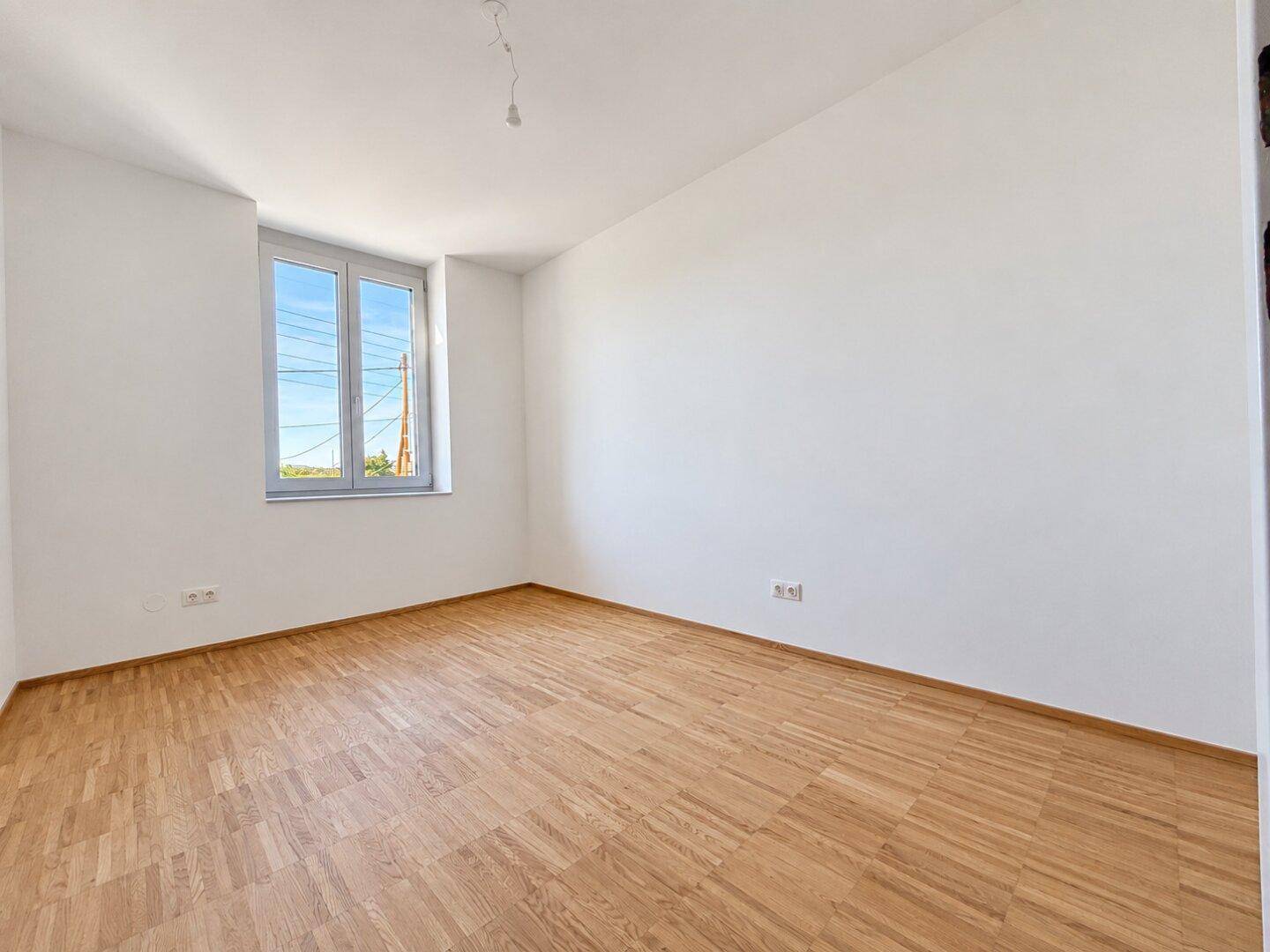 Geräumiges, leeres Schlafzimmer mit Parkettboden und einem Fenster, das für gute Belichtung sorgt.
