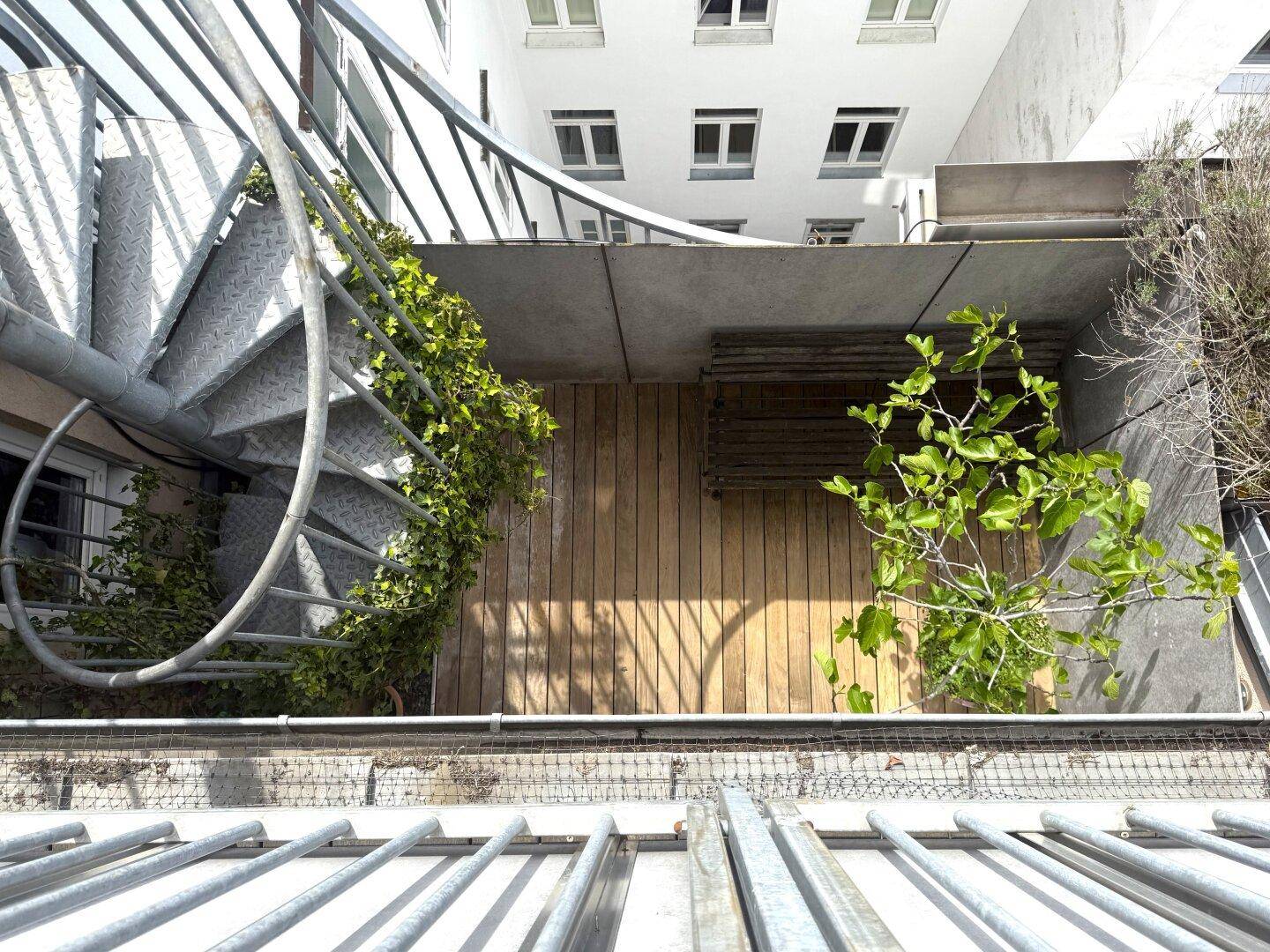 Detailansicht einer Terrasse mit Holzbelag, Wendeltreppe und grüner Bepflanzung.