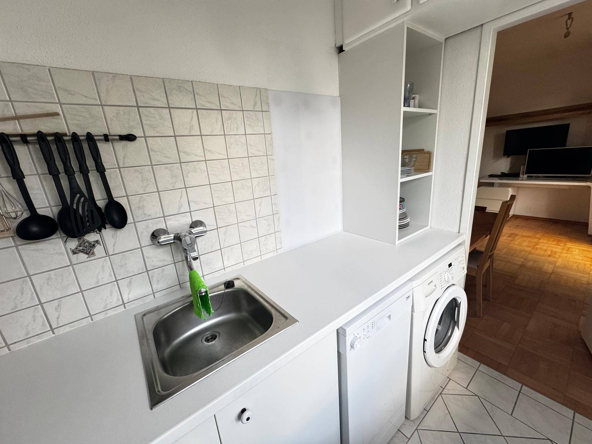 Küchenzeile mit Spüle, Arbeitsplatte, Geschirrspüler und Blick in den Wohnbereich.