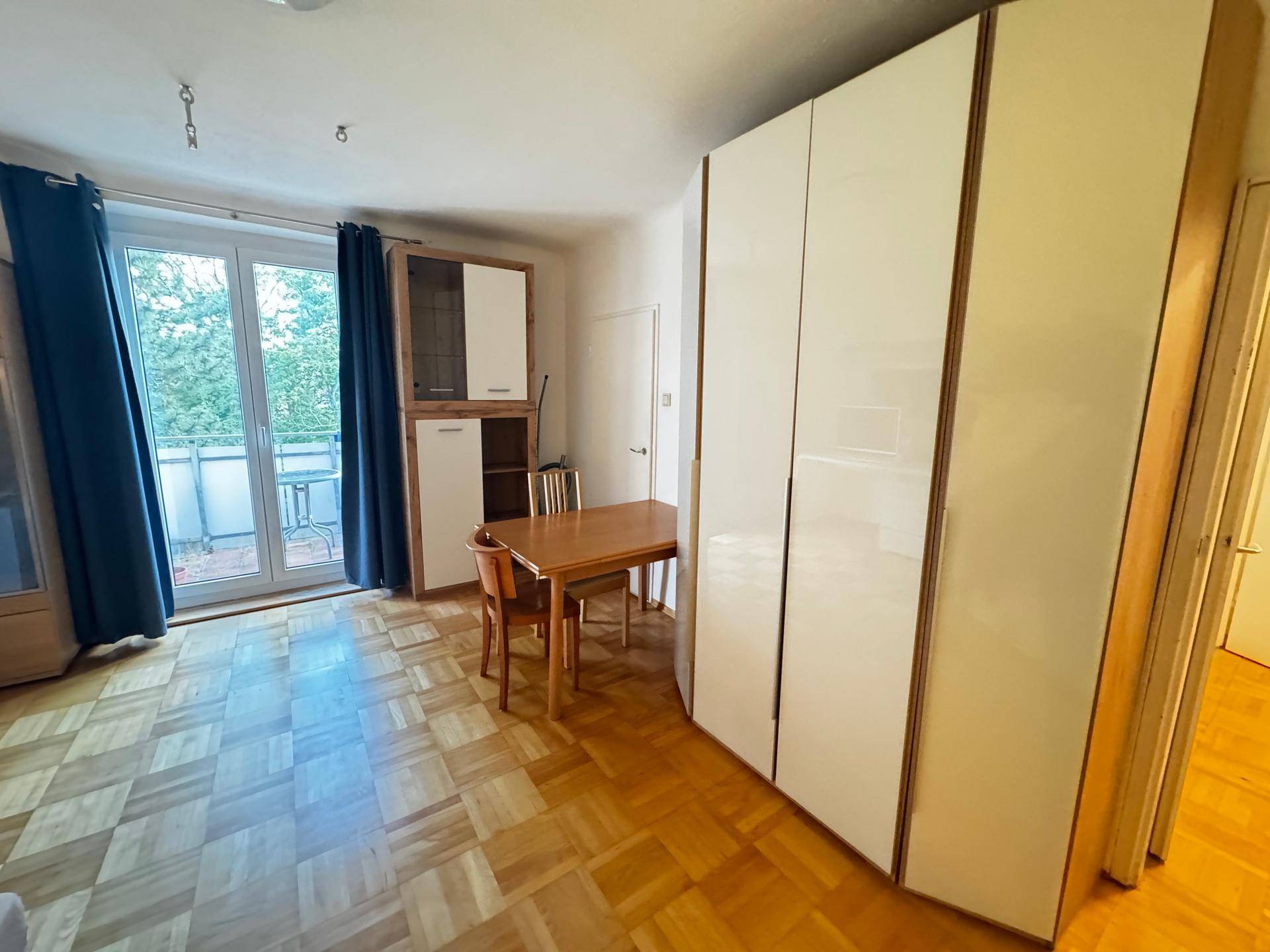 Geräumiges Studio-Apartment mit Parkettboden, Essbereich und großen Einbauschränken.