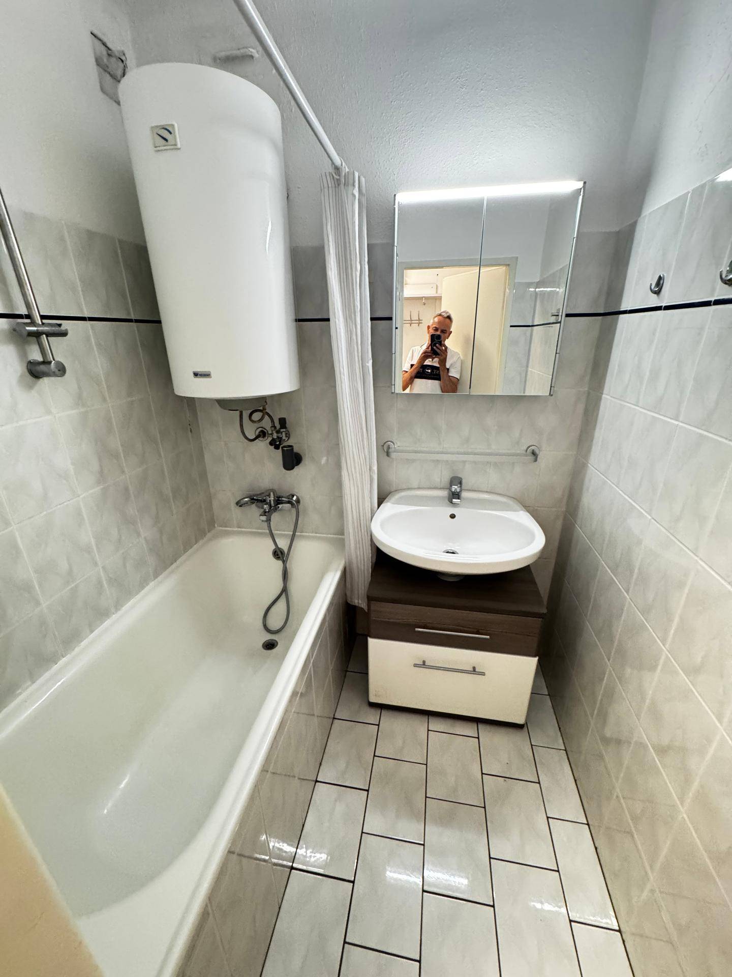 Badezimmer mit Badewanne, Waschbecken, Spiegelschrank und hellen Fliesen.