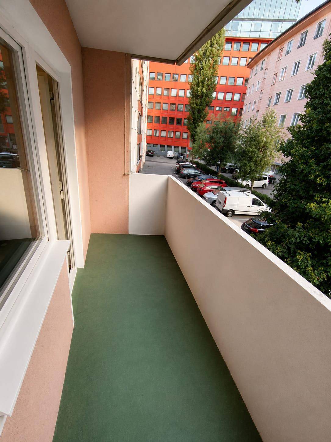 Balkon mit Blick auf umliegende Gebäude und parkende Autos.