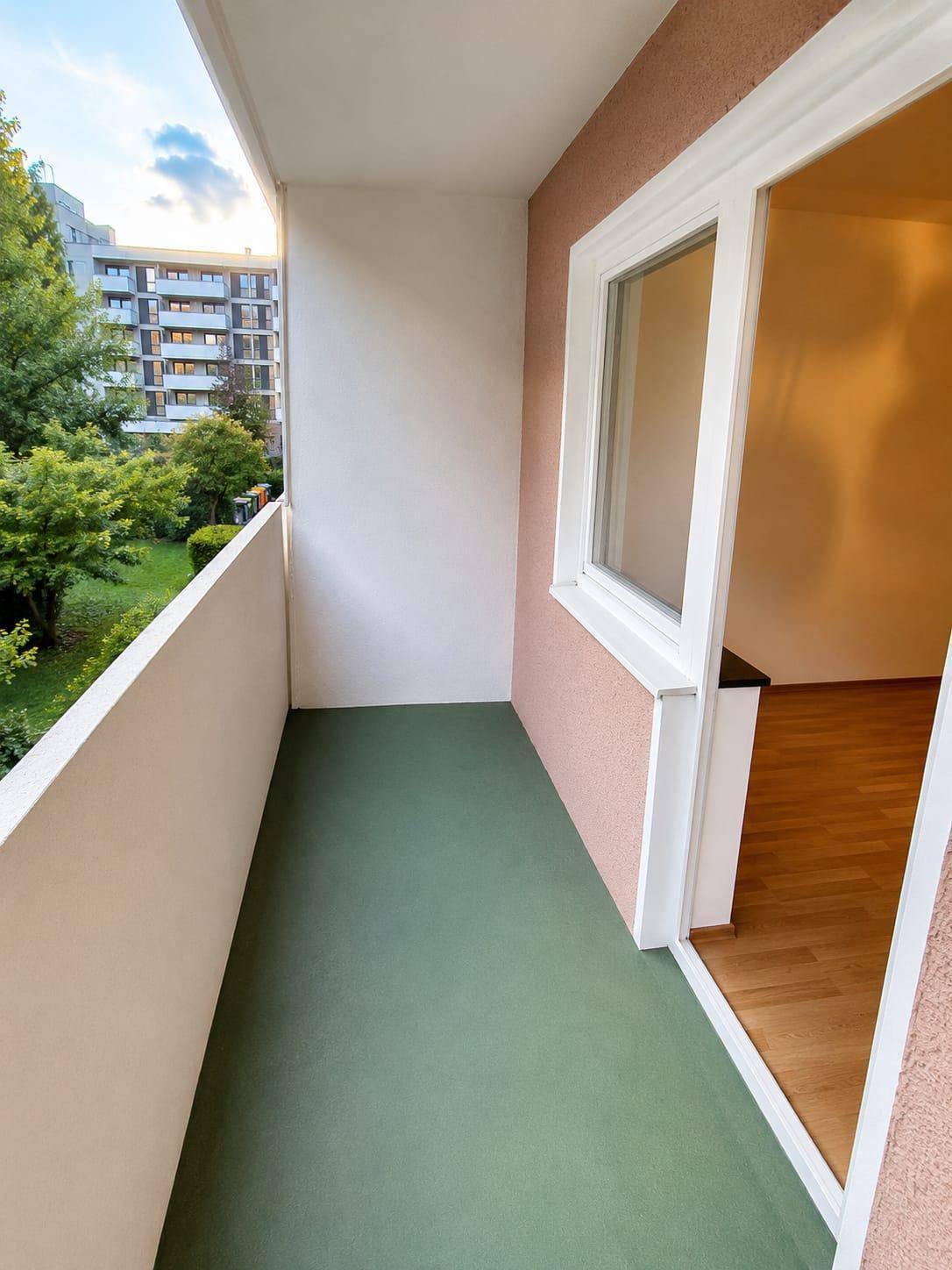 Geräumiger Balkon mit Blick auf grüne Bäume und weitere Gebäude.