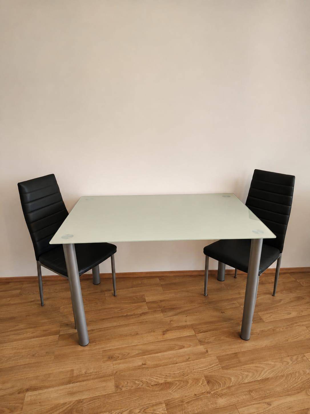 Kleiner Esstisch mit Glasplatte und zwei modernen Stühlen für gemütliche Mahlzeiten.