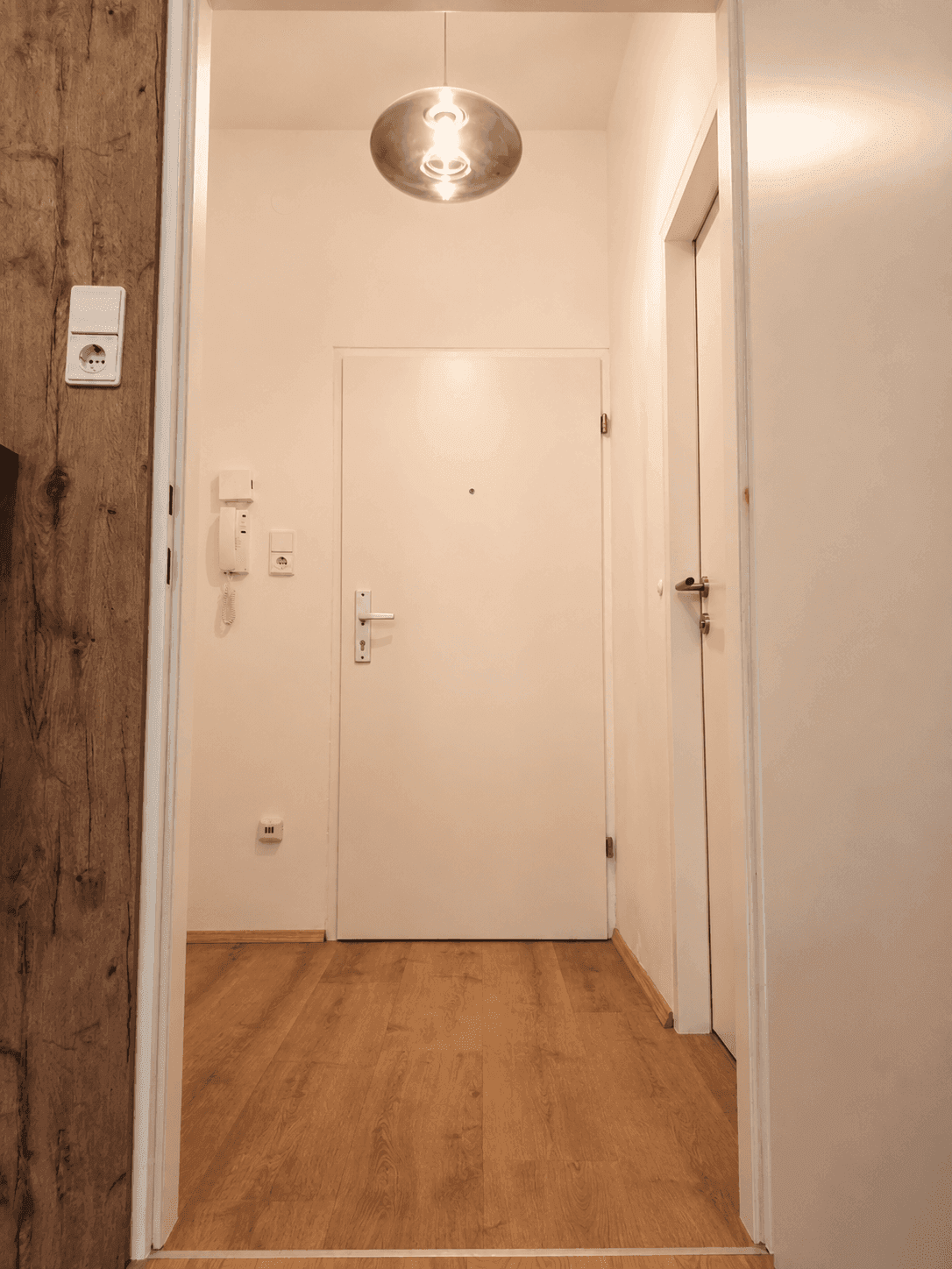 Heller Eingangsbereich mit Holzboden und Gegensprechanlage.