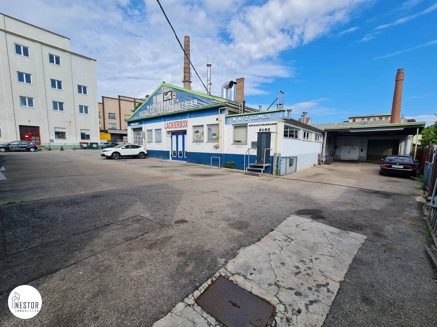 Gewerbegebäude mit Lackierbox-Bereich und einem Schornstein, umgeben von einem geräumigen Parkplatz.