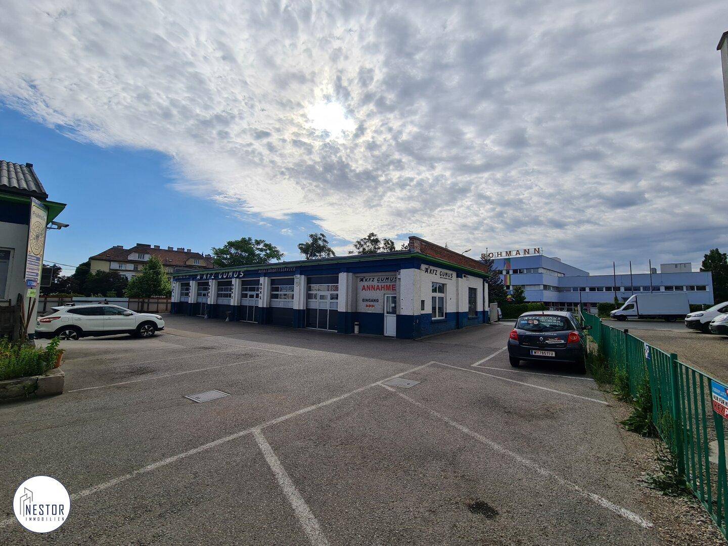 Weitläufige Außenansicht des Gewerbegebäudes mit großem Parkplatz unter einem teilweise bewölkten Himmel.