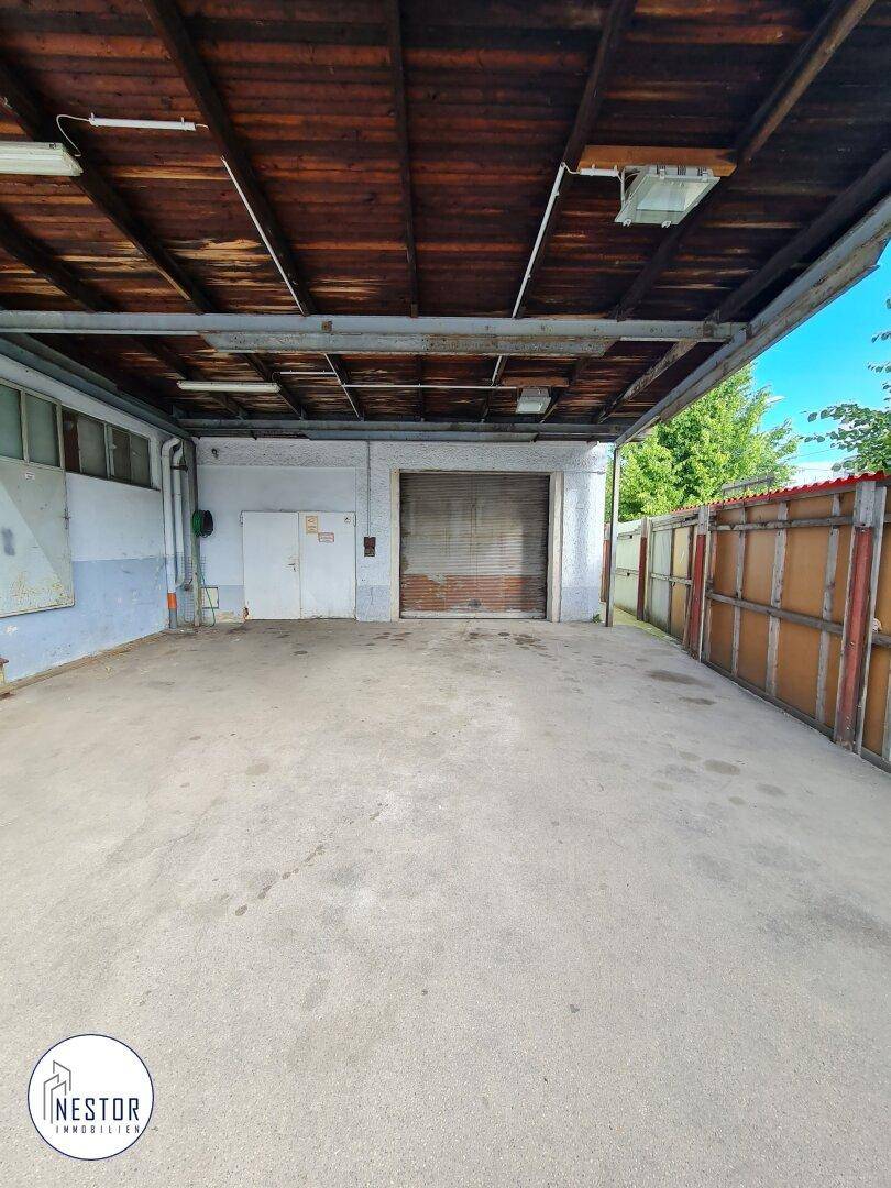 Überdachter Außenbereich, möglicherweise eine Laderampe oder Garagenerweiterung, mit Rolltor und Holzdecke.