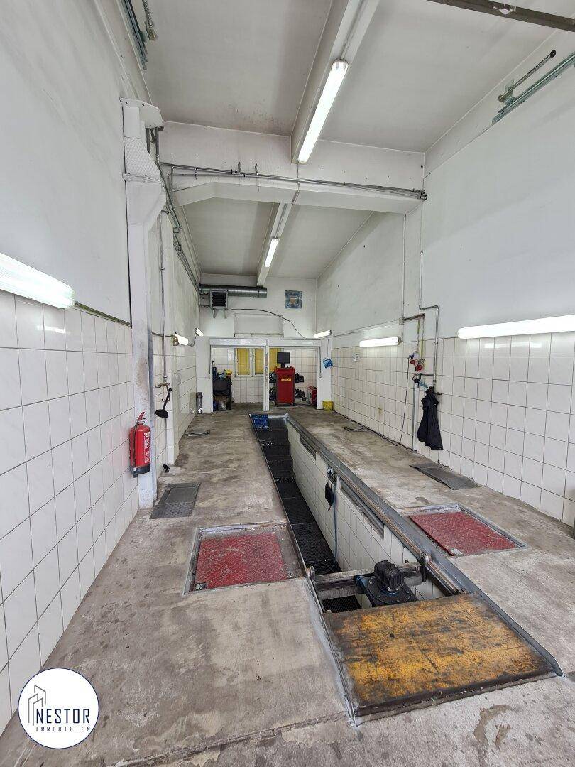 Innenansicht eines Servicegrubenbereichs mit gefliesten Wänden und Betonboden, Feuerlöscher sichtbar.