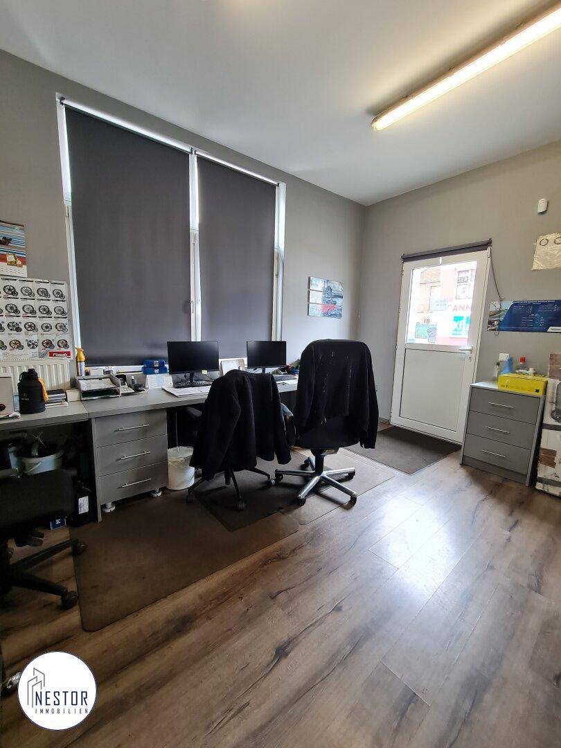 Innenansicht eines Büroraums mit zwei Schreibtischen, Stühlen und Computern, Fenster mit Jalousien.