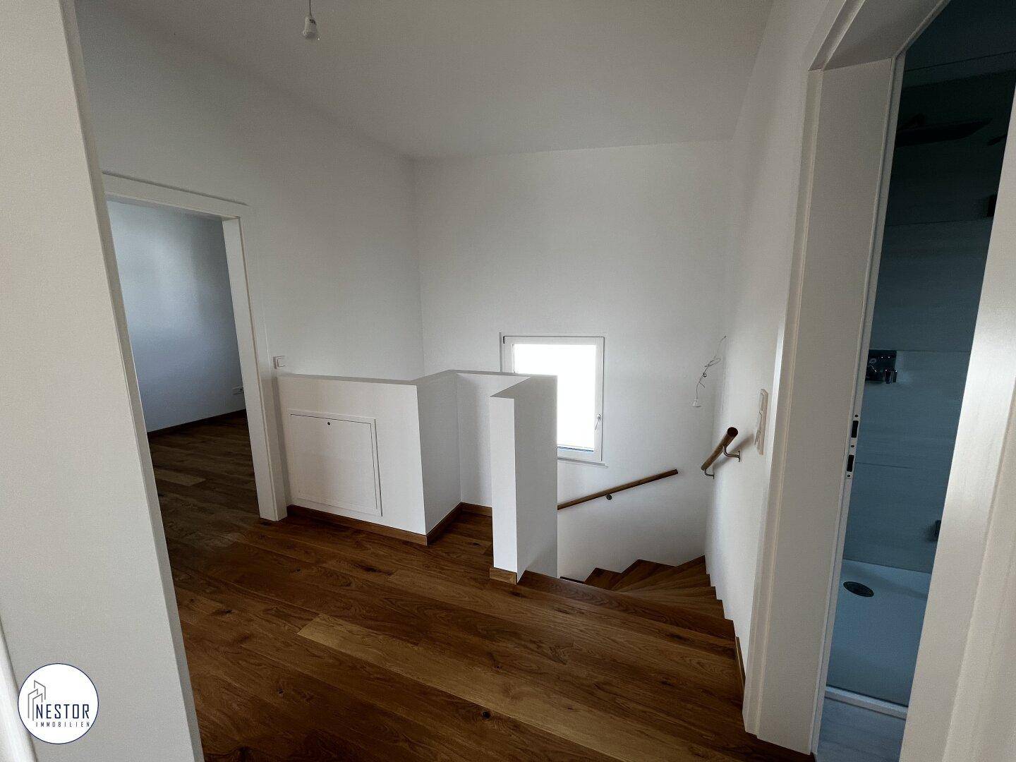 Heller Flurbereich mit Holztreppe und kleinem Fenster, das den Raum erhellt.