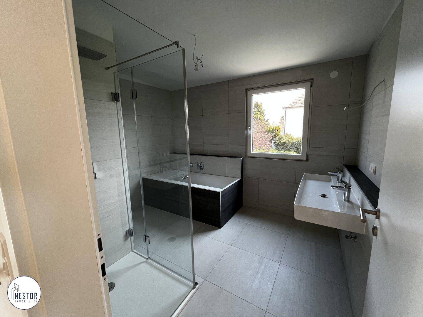 Modernes Badezimmer mit Dusche, Badewanne, Doppelwaschbecken und Fenster für Tageslicht.