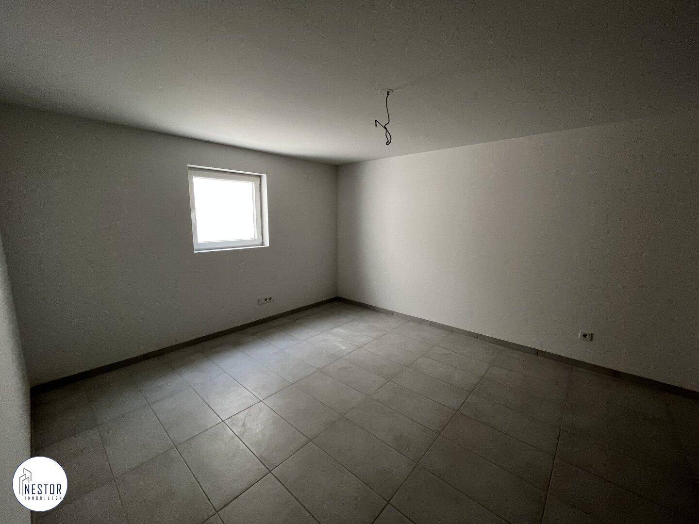 Heller, unmöblierter Raum im Untergeschoss mit Fenster und Fliesenboden.
