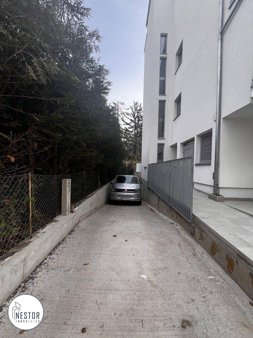 Zufahrt zum Gebäude mit einem geparkten Fahrzeug und seitlichem Zugang.