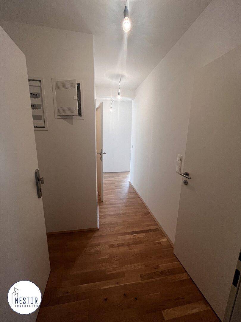 Langer, heller Flur mit Holzboden und weißen Wänden, der zu weiteren Räumen führt.