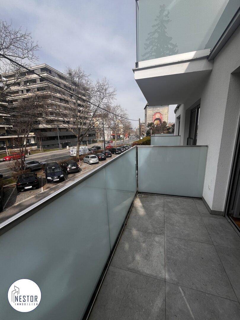 Balkon mit Glasbrüstung und Fliesenboden, bietet Blick auf die belebte Straße.