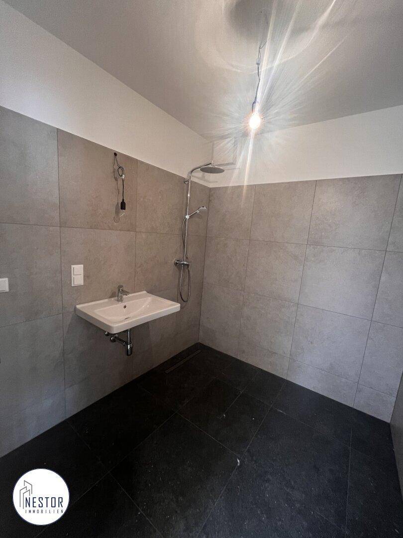 Modernes Badezimmer mit Dusche, Waschbecken und großformatigen grauen Fliesen.