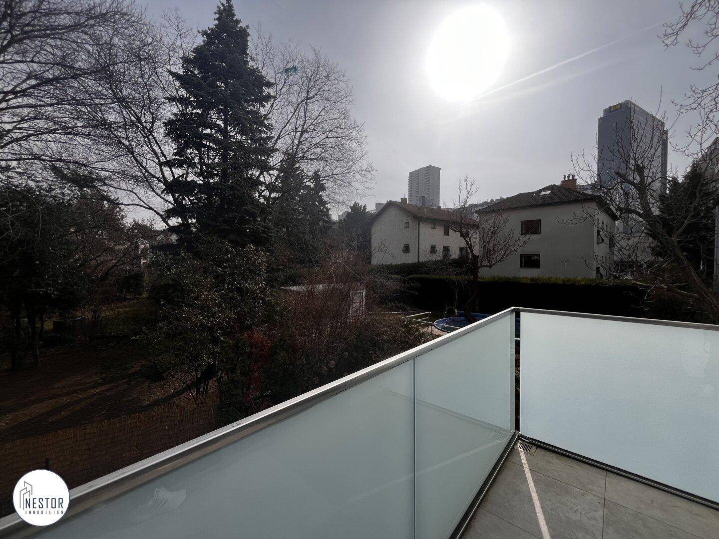 Sonniger Balkon mit Glasbrüstung und weitem Blick ins Grüne und auf die Stadt.