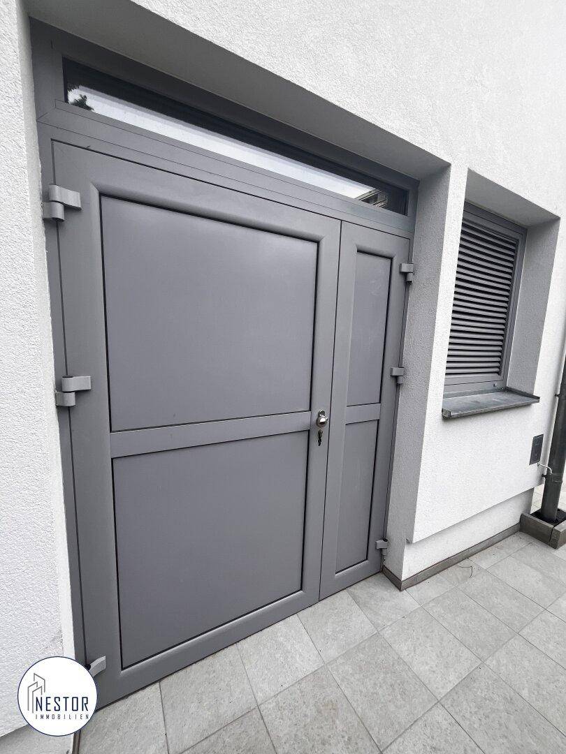 Graue Eingangstür und Fenster mit Rollladen an der modernen Gebäudefassade.