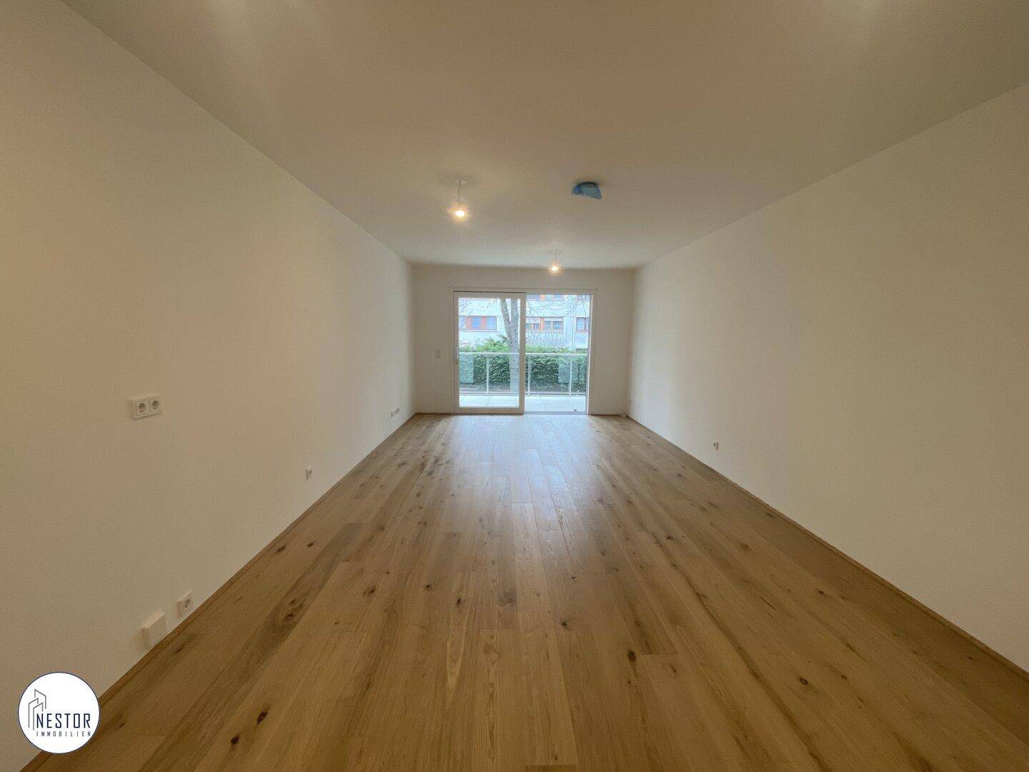 Geräumiges Wohnzimmer mit Holzboden und Zugang zu einem Balkon oder einer Terrasse.