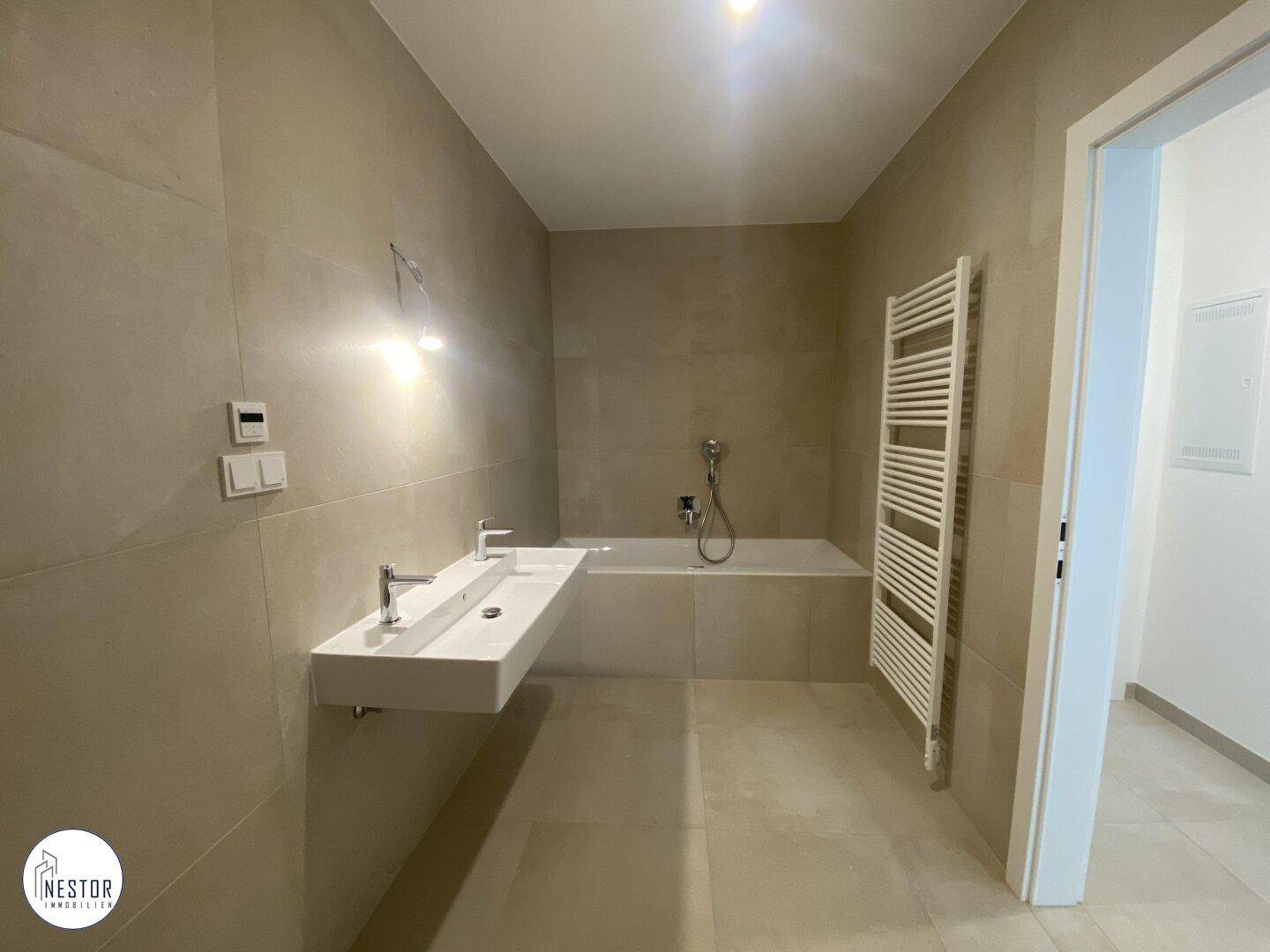 Modernes Badezimmer mit beigen Fliesen, Doppelwaschbecken, Badewanne und beheiztem Handtuchhalter.