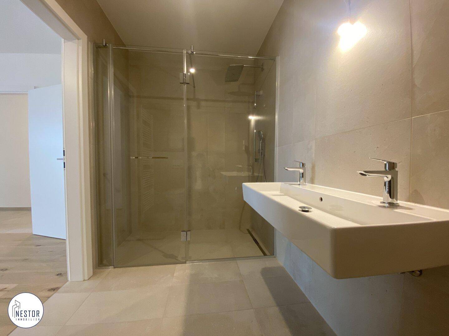 Modernes Badezimmer mit beigen Fliesen, Doppelwaschbecken und geräumiger begehbarer Dusche.