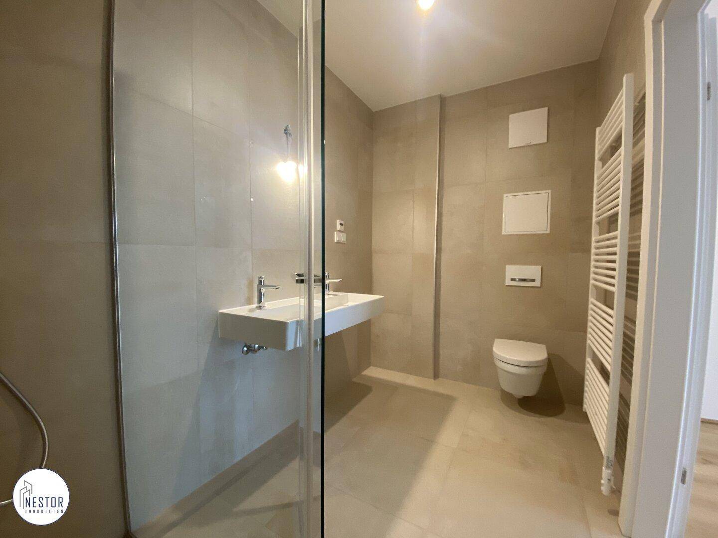 Modernes Badezimmer mit beigen Fliesen, wandhängendem WC, Einzelwaschbecken und beheiztem Handtuchhalter.