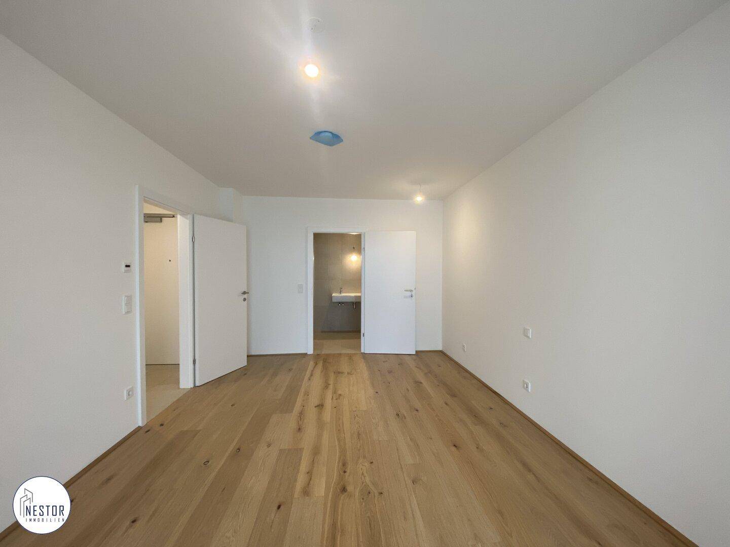 Helles Schlafzimmer mit Holzboden und Zugang zu einem modernen Badezimmer.