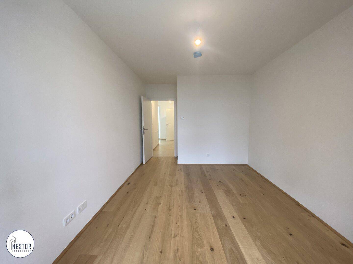 Helles Zimmer mit Holzboden und weißen Wänden, ideal als Schlafzimmer oder Arbeitszimmer.