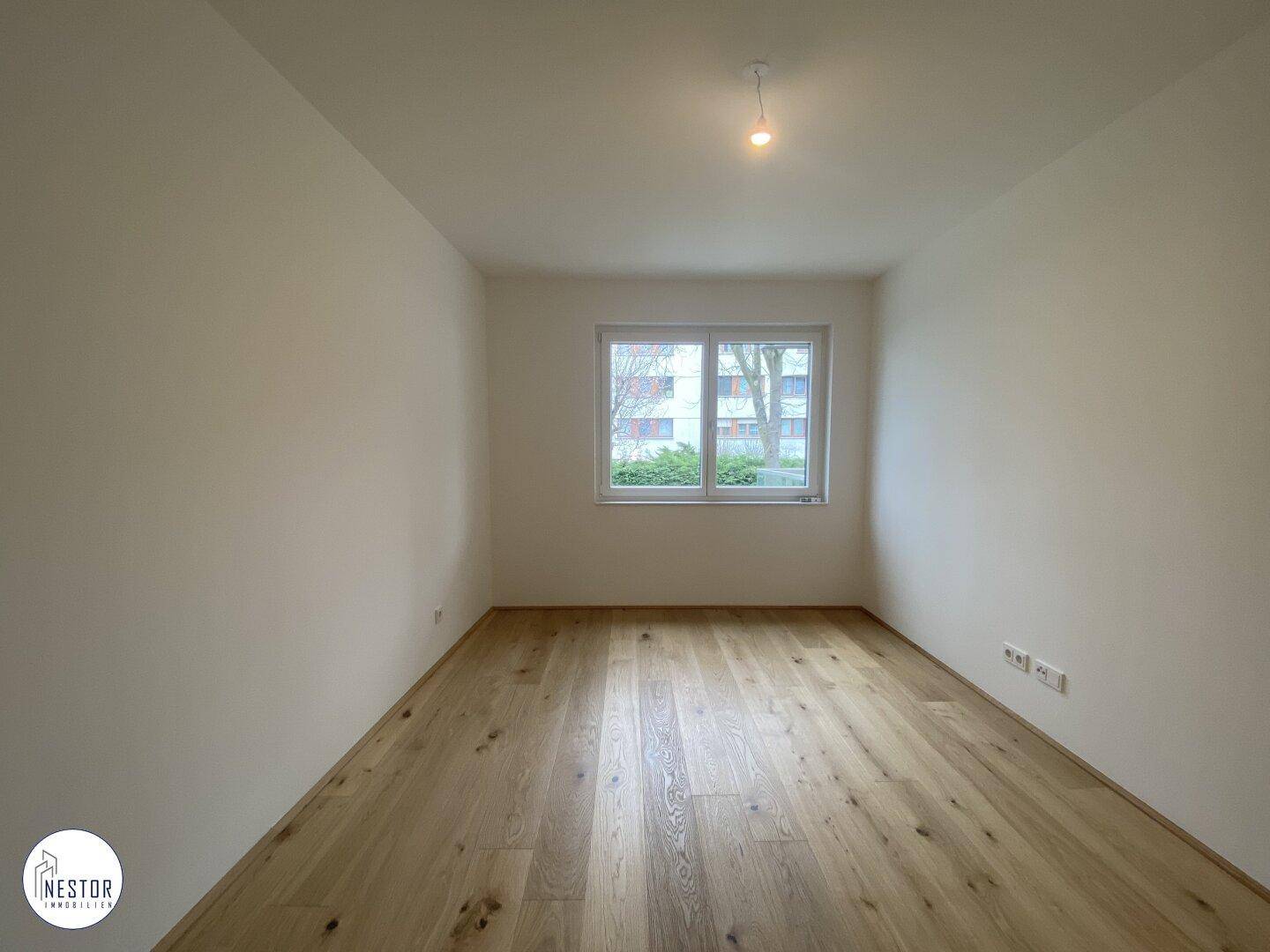 Helles Schlafzimmer mit Holzboden und Fenster, das einen Blick ins Grüne bietet.