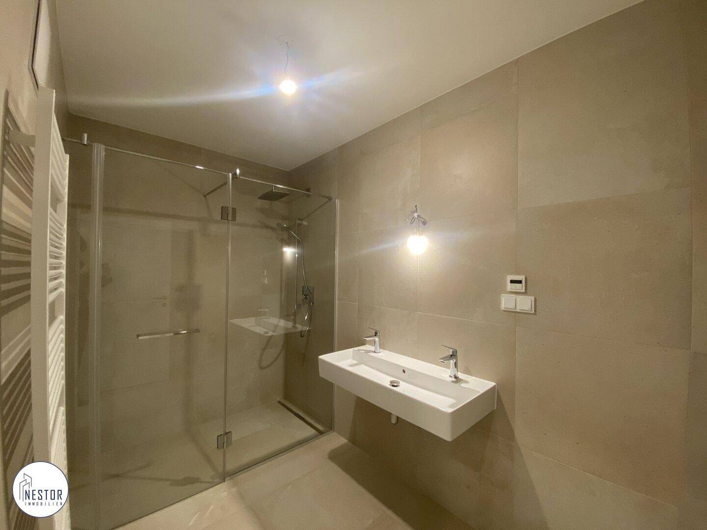 Elegantes Badezimmer mit großformatigen Fliesen, moderner Dusche und zwei Waschbecken.