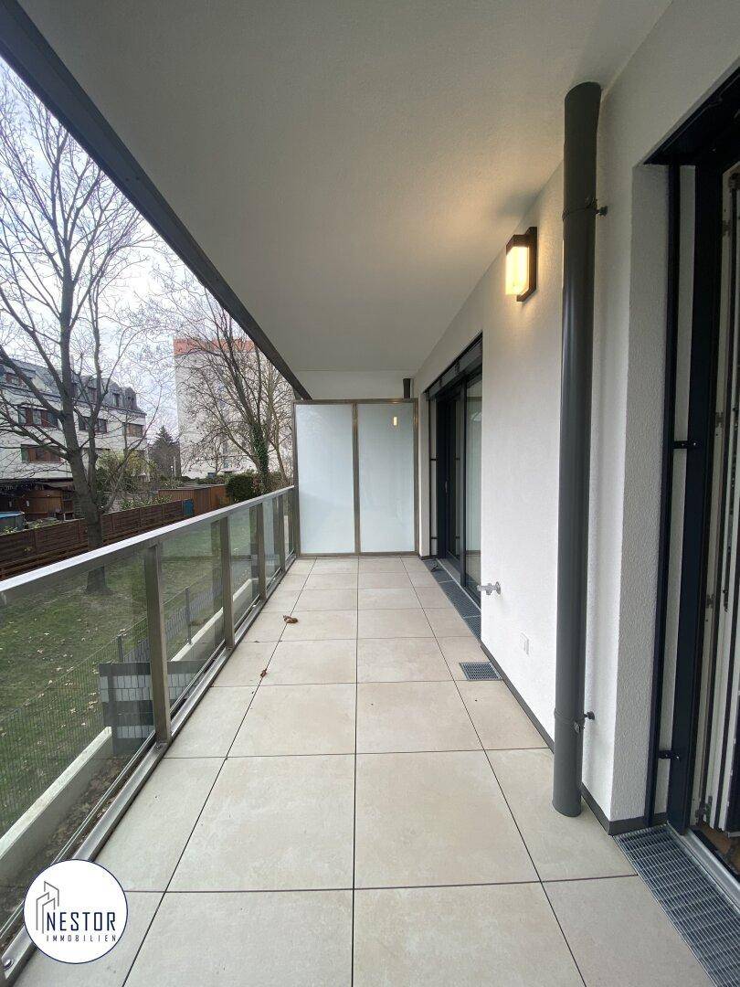 Geräumiger Balkon mit Fliesenboden, Glasgeländer und Blick ins Grüne.
