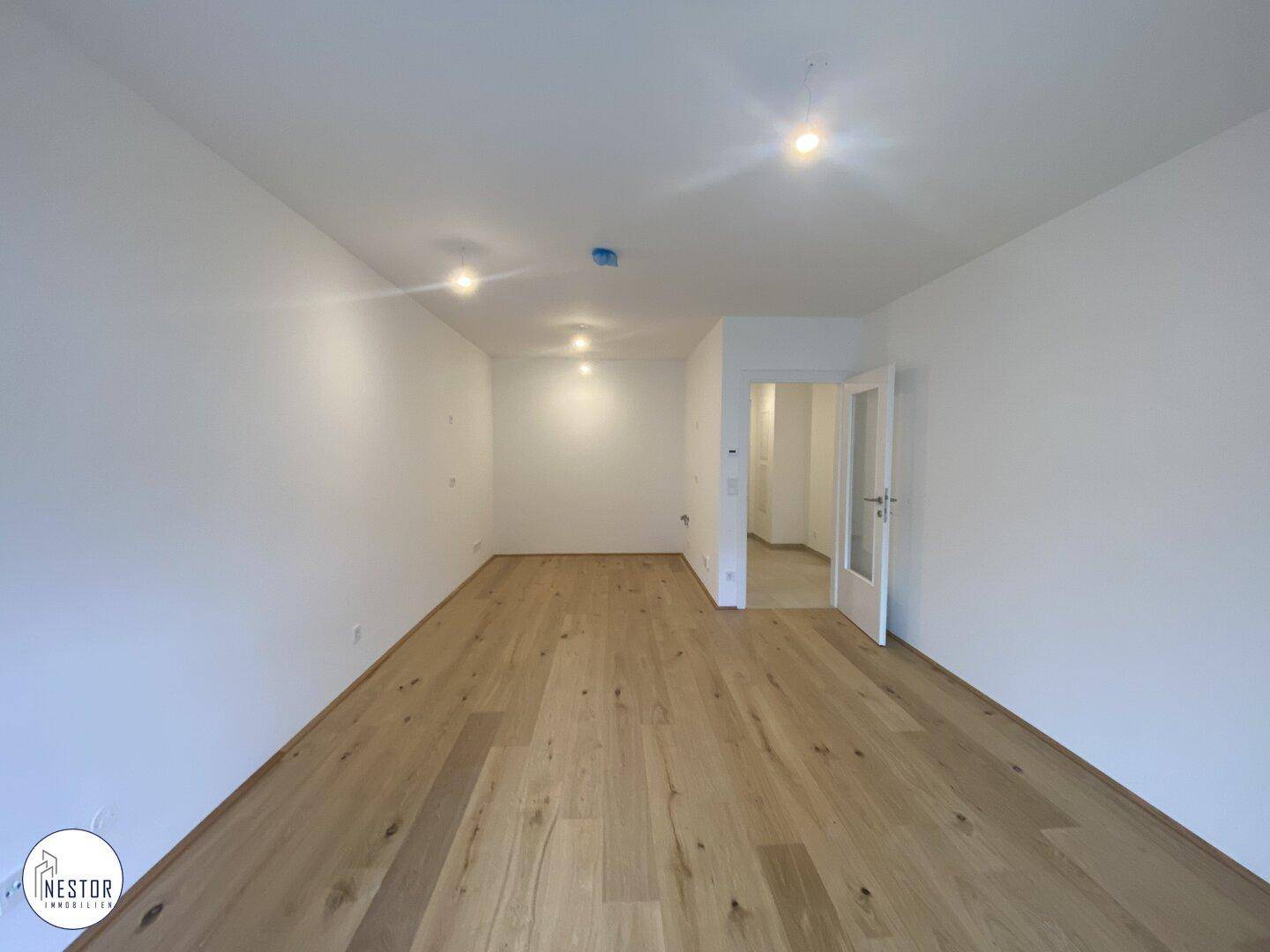 Geräumiges, leeres Wohnzimmer mit hellem Parkettboden und Zugang zu einem weiteren Raum.