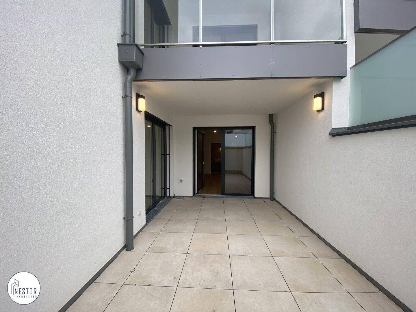 Geräumige, geflieste Terrasse im Erdgeschoss mit direktem Zugang zum Gebäude und Außenbeleuchtung.