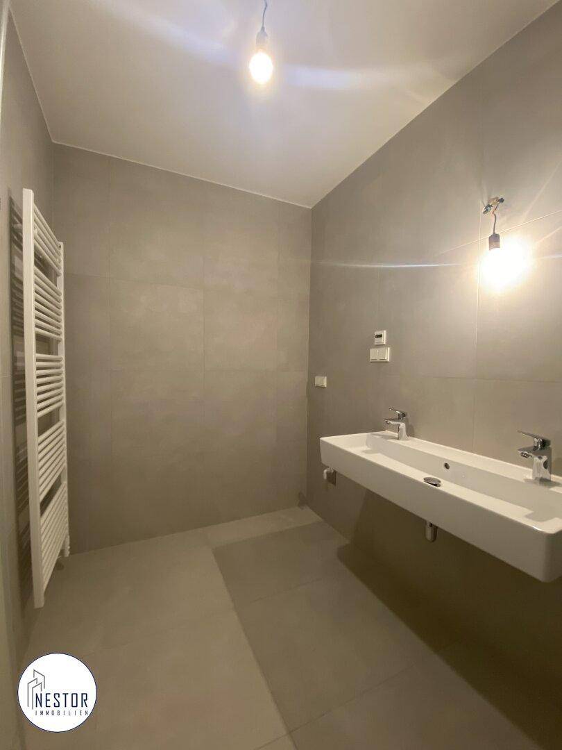 Modernes Badezimmer mit doppelten Waschbecken, grauen Fliesen und einem beheizten Handtuchhalter.