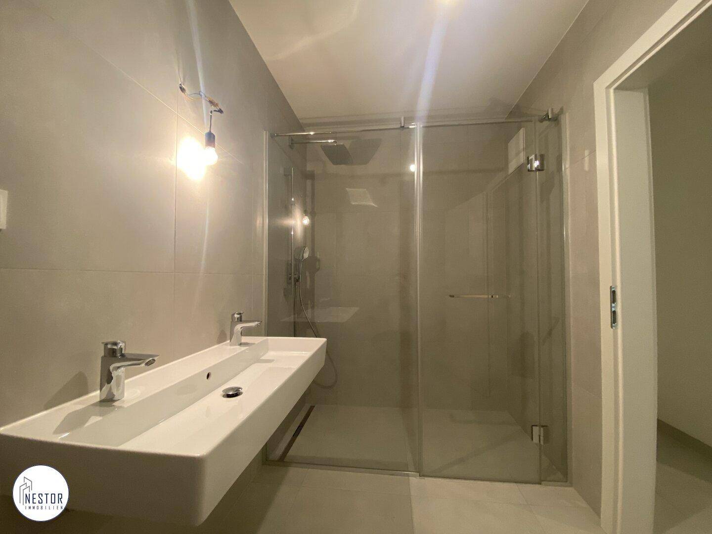 Elegantes Badezimmer mit Doppelwaschbecken, großer begehbarer Dusche und modernen grauen Fliesen.